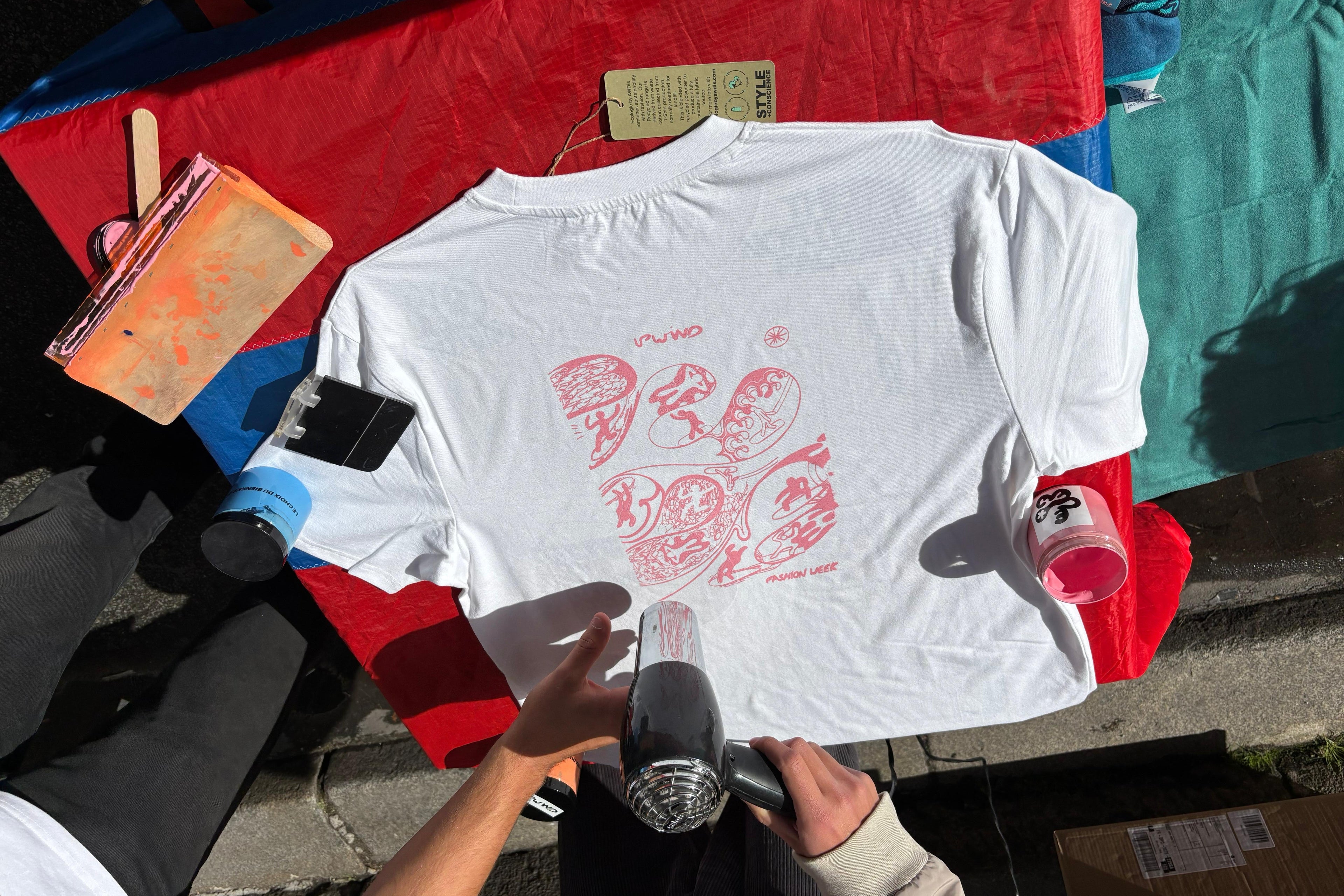Finished custom screenprinted white t-shirt held up at UPWIND recycled serigraphy fashion event